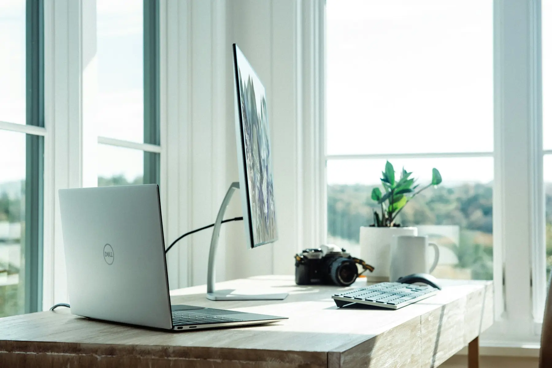 Tidy desk by a bright window with a laptop and monitor