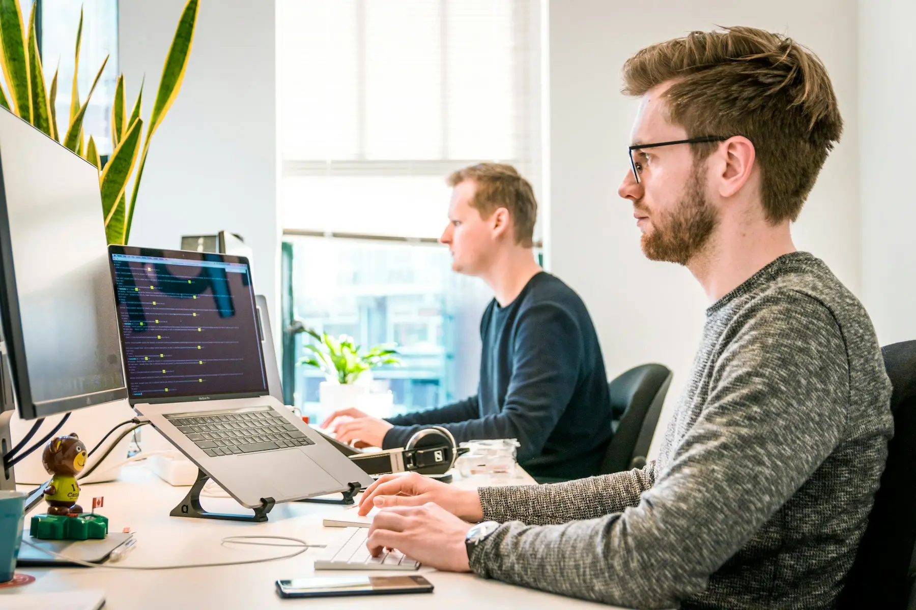 Two people working side by side at computers in a bright office