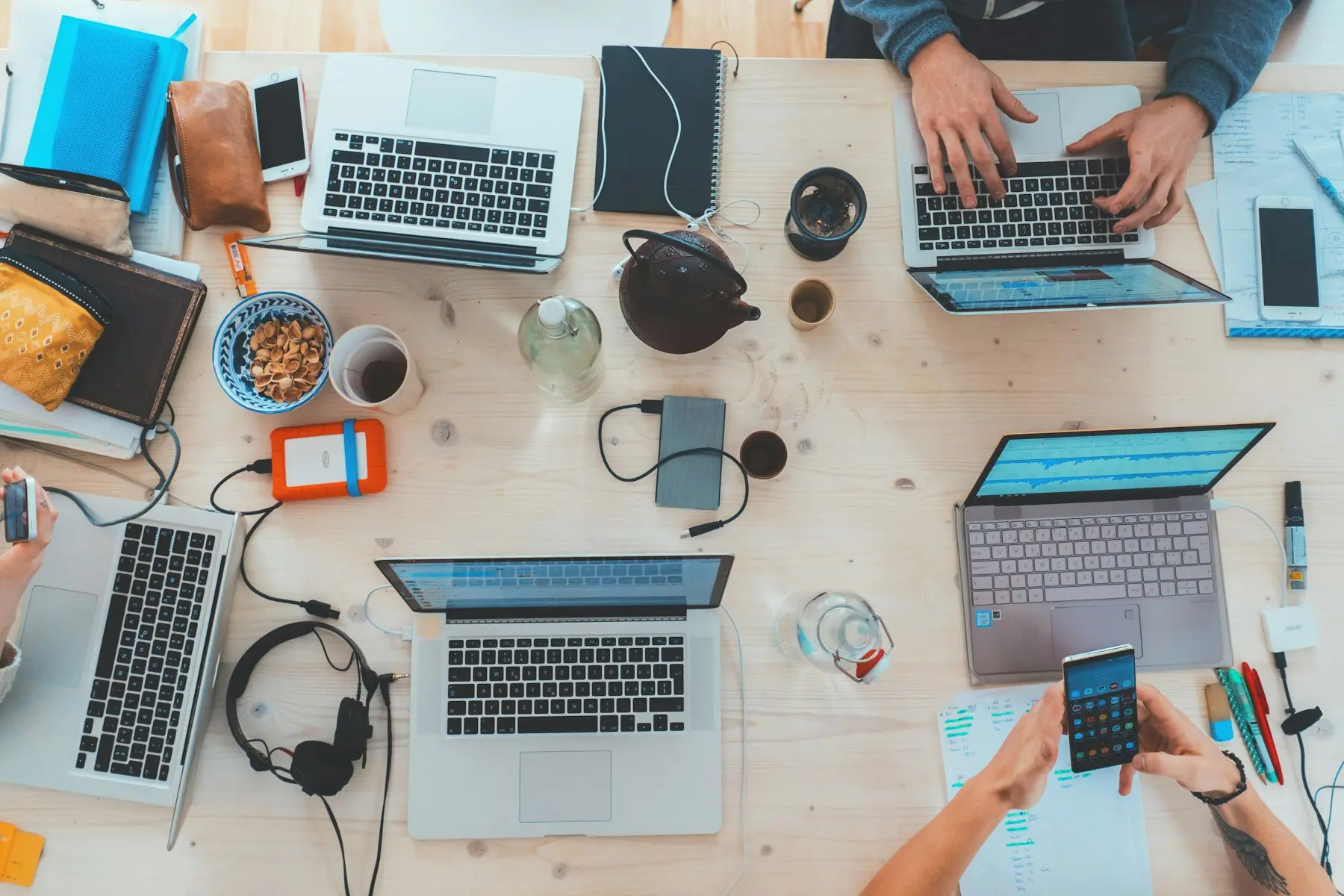Overhead view of a shared desk with laptops, notebooks and phones